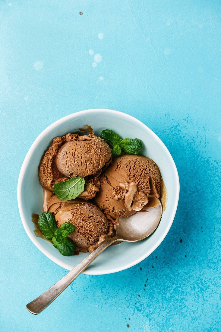 Chocolate ice cream with mint leaf in bowl on blue background