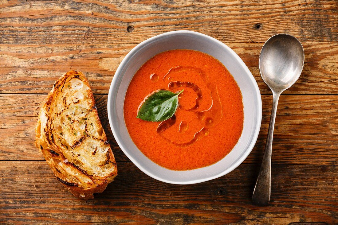 Tomaten-Gazpacho mit Röstbrot auf Holzuntergrund (Aufsicht)