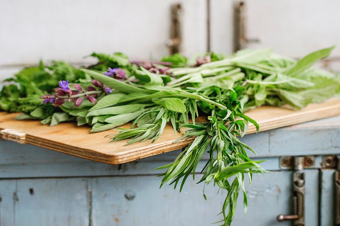 Assortment of fresh herbs mint, oregano, thym, blooming sage on cutting board over old blue white wooden kitchen table