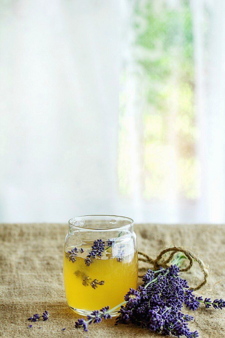 Organic raw honey in glass jar flavored with lavender flowers, standing on table with sackcloth