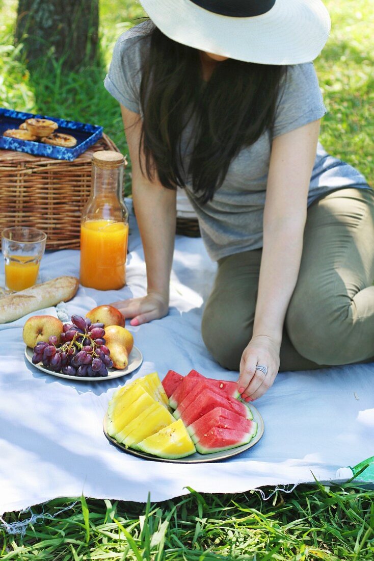 Junge Frau sitzt auf Picknickdecke im Park und isst Wassermelone