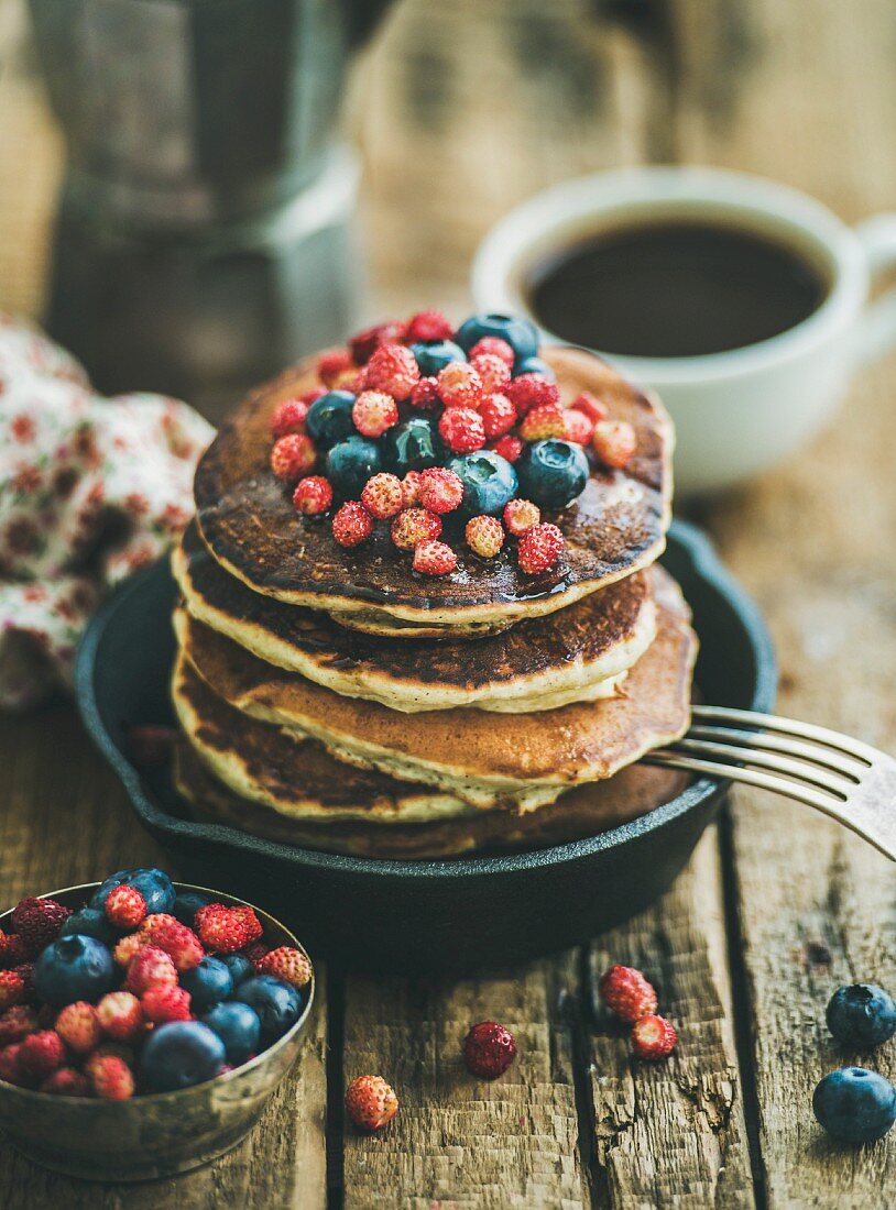 Sweet breakfast with pancakes with fresh forest berries and honey in cast iron pan over rustic wooden background