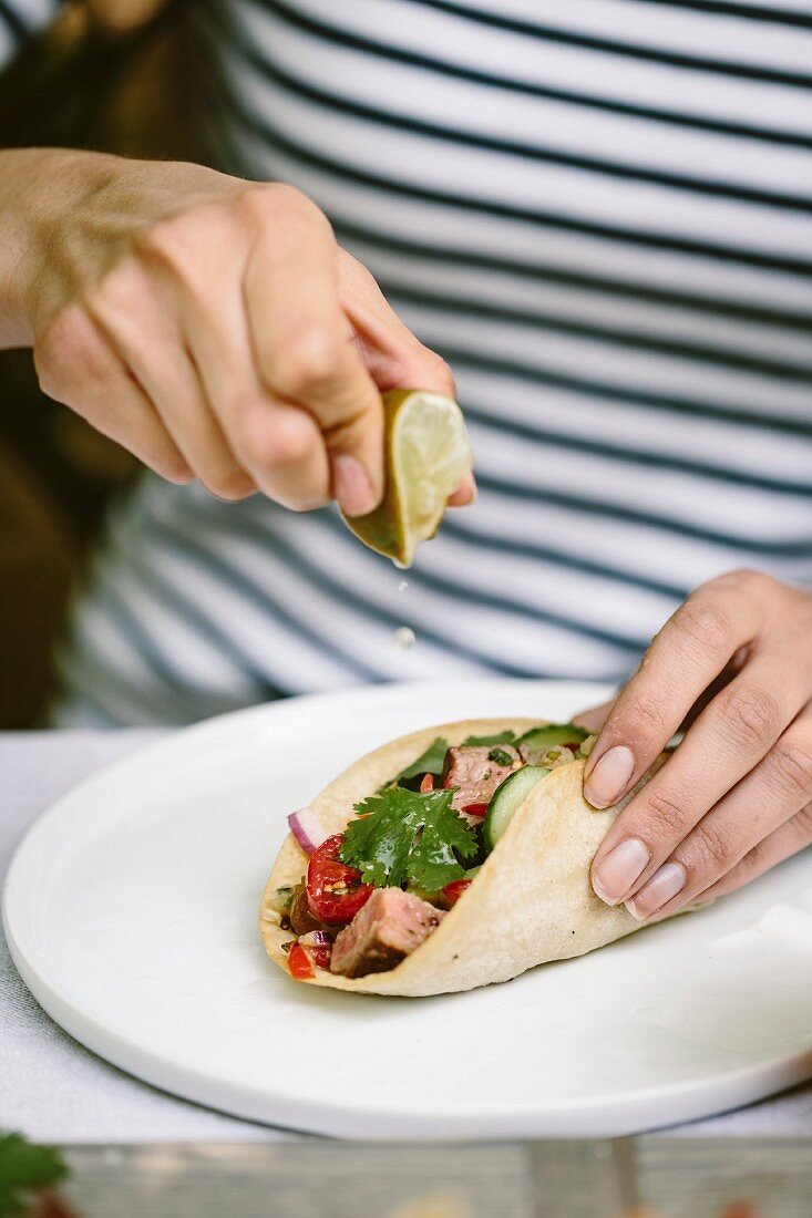Frau träufelt Limettensaft auf Taco mit gegrilltem Flank Steak