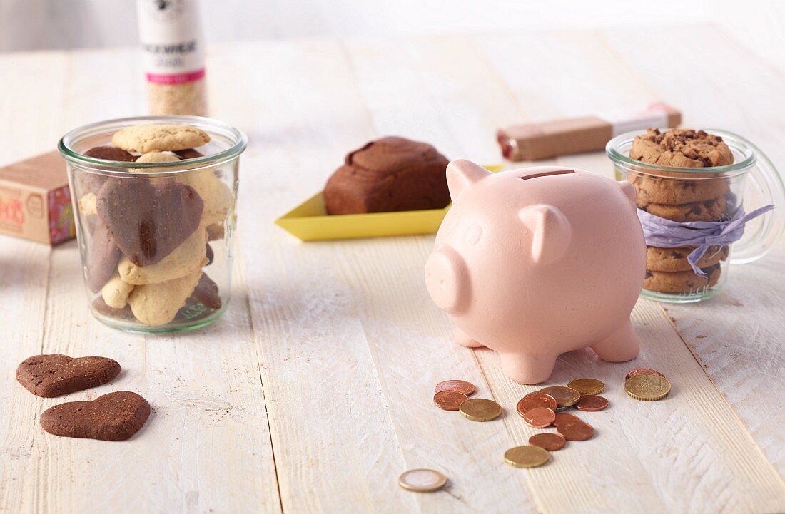 Kekse und Sparschwein mit Münzen auf Holztisch