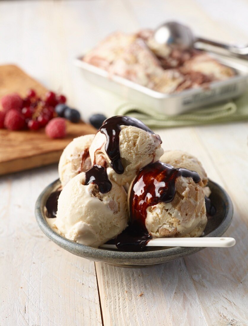 Ice cream with chocolate sauce, with fresh berries in the background