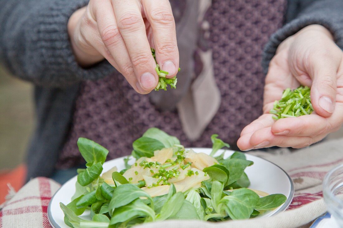 Einen Topinambursalat mit Schnittlauch bestreuen