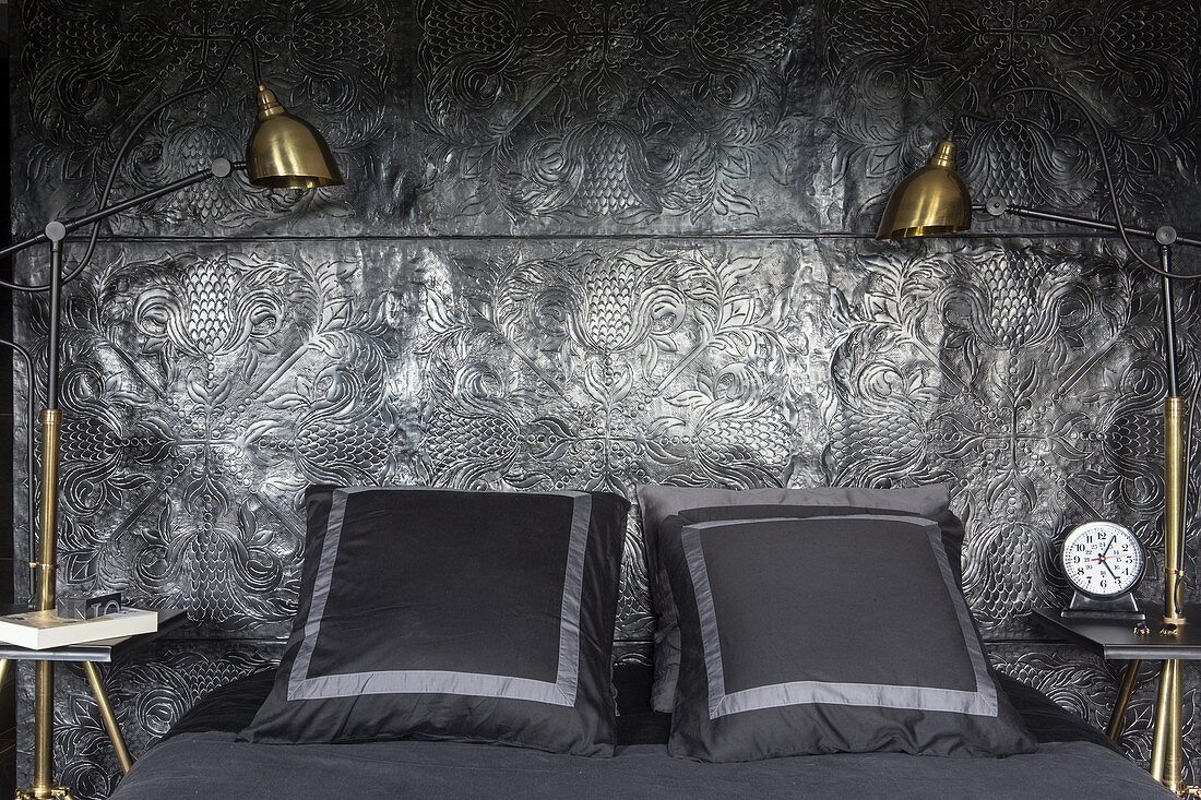 Double bed against black relief wall with gilt bedside lamps