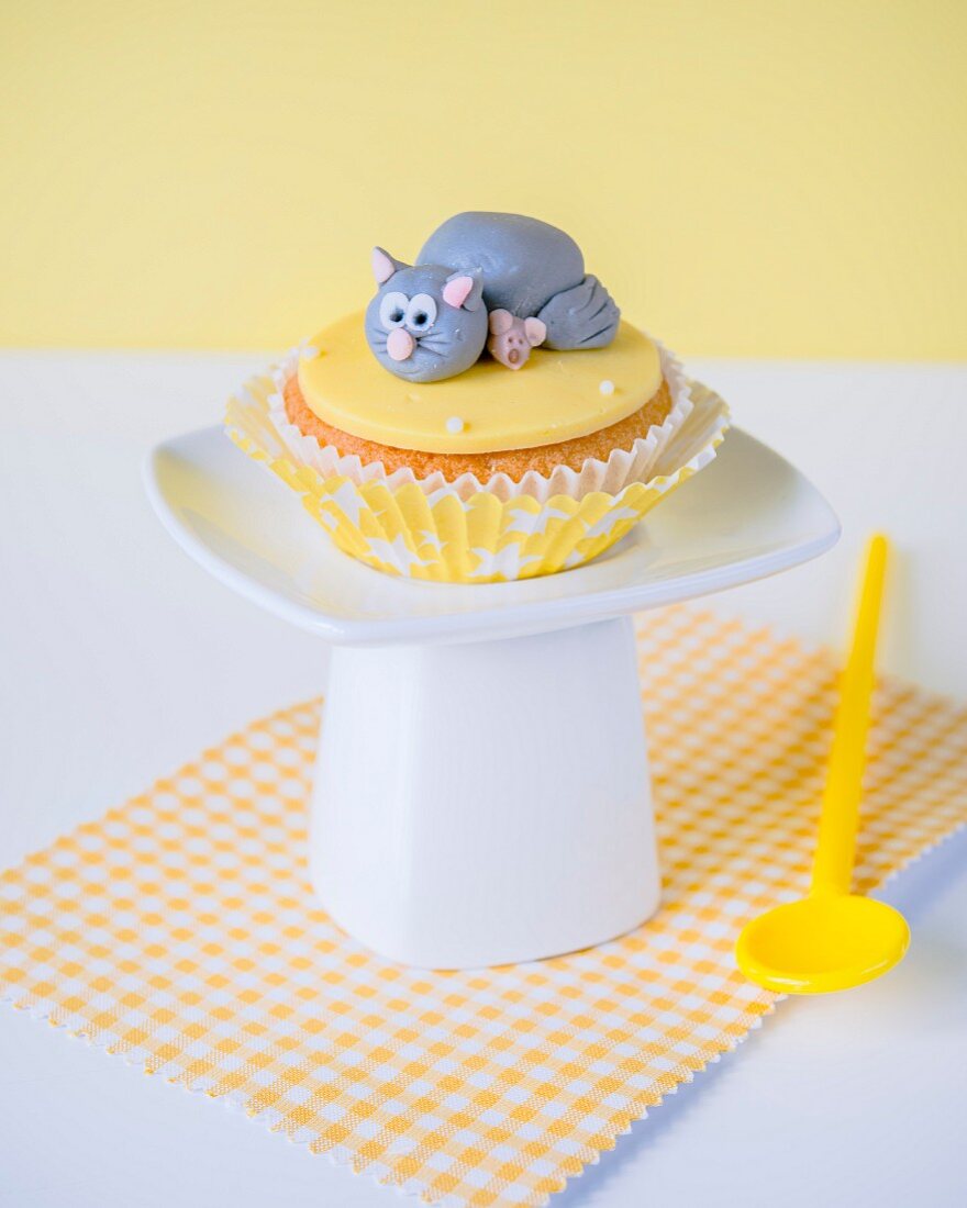 A cupcake with a fondant icing cat and mouse on the top