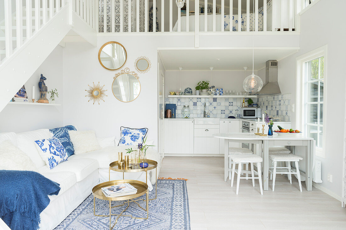 Offener Wohnraum mit weißer Couch, weißem Esstisch und Küche unter Galerie
