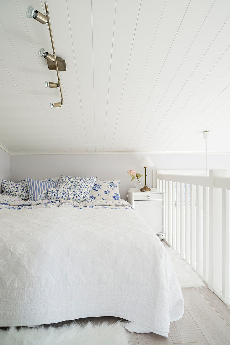 Double bed with white bedspread and white and blue scatter cushions on gallery