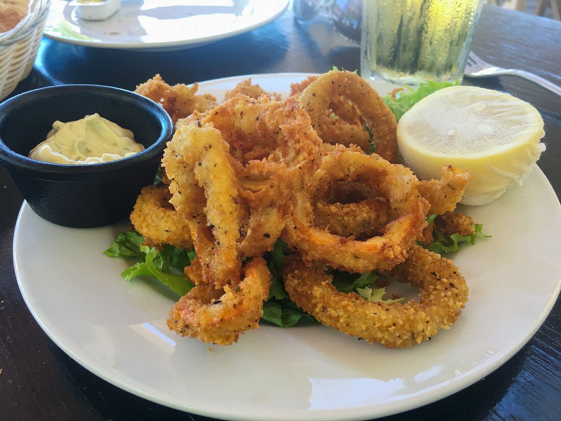 A serving of fried calamari rings on a white plate with a lemon and dipping sauce
