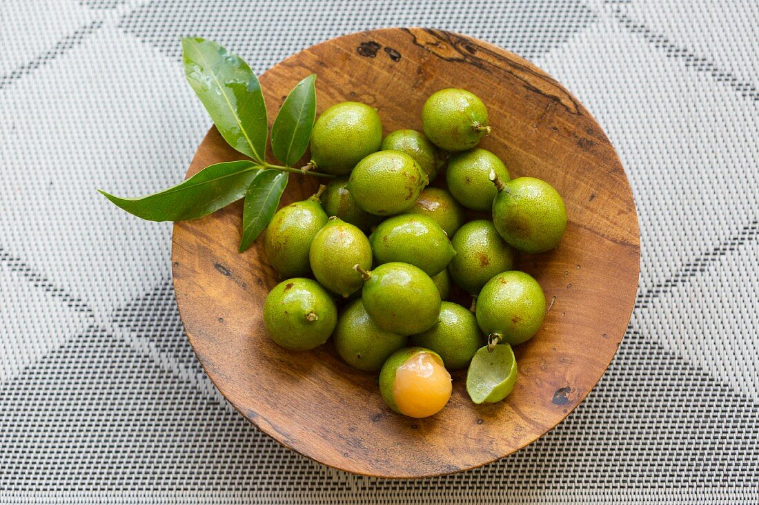 Quenepas (also known as Spanish Limes, genip or Kenips) in a small wodden bowl on a gray surface