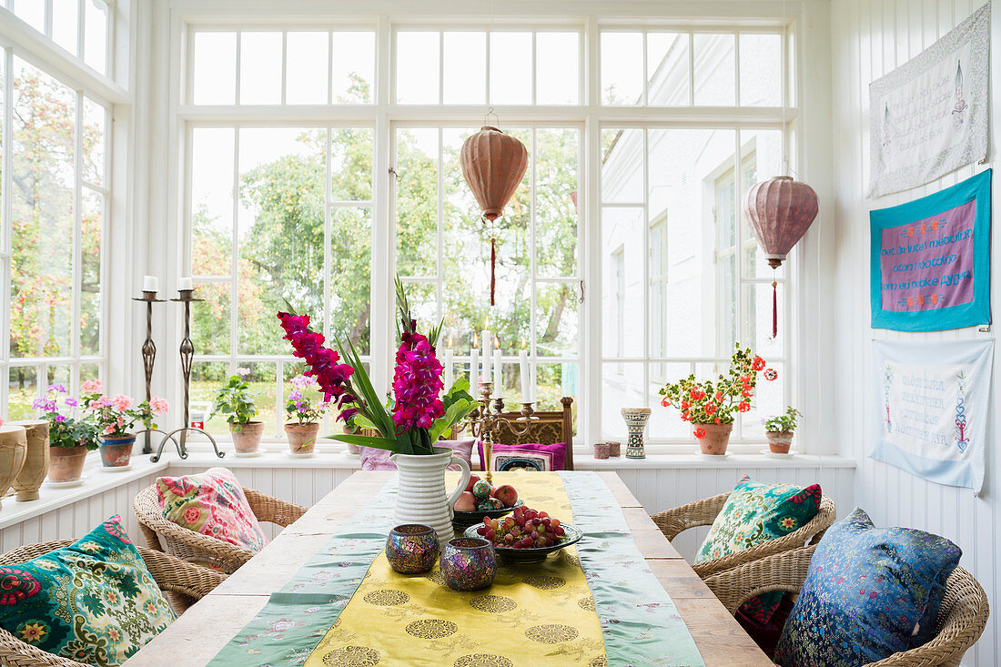 Runner and flowers on dining table with rattan armchairs and potted plants in conservatory