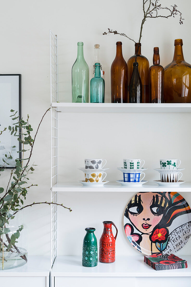 Green and brown bottles and china on String shelves in kitchen