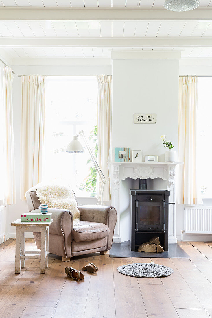 Fur blanket on leather armchair in front of log burner in bright living room