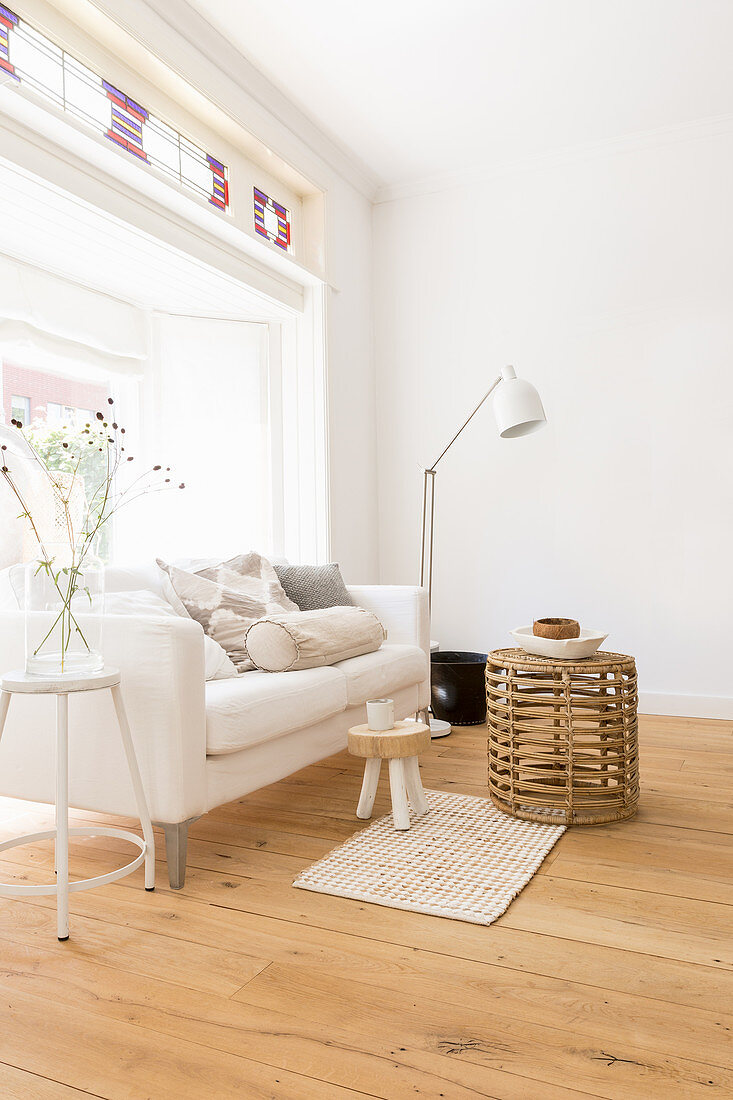 White sofa, standard lamp and wicker coffee table in front of window bay