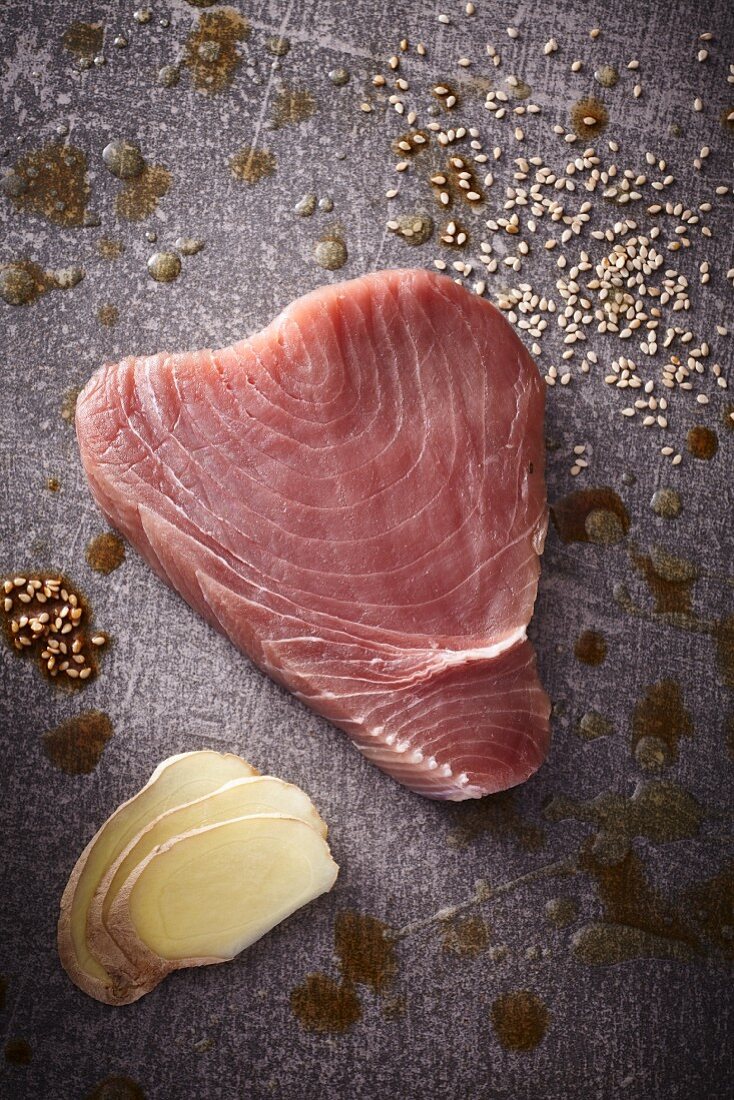 A raw tuna steak with sesame seeds and slices of ginger
