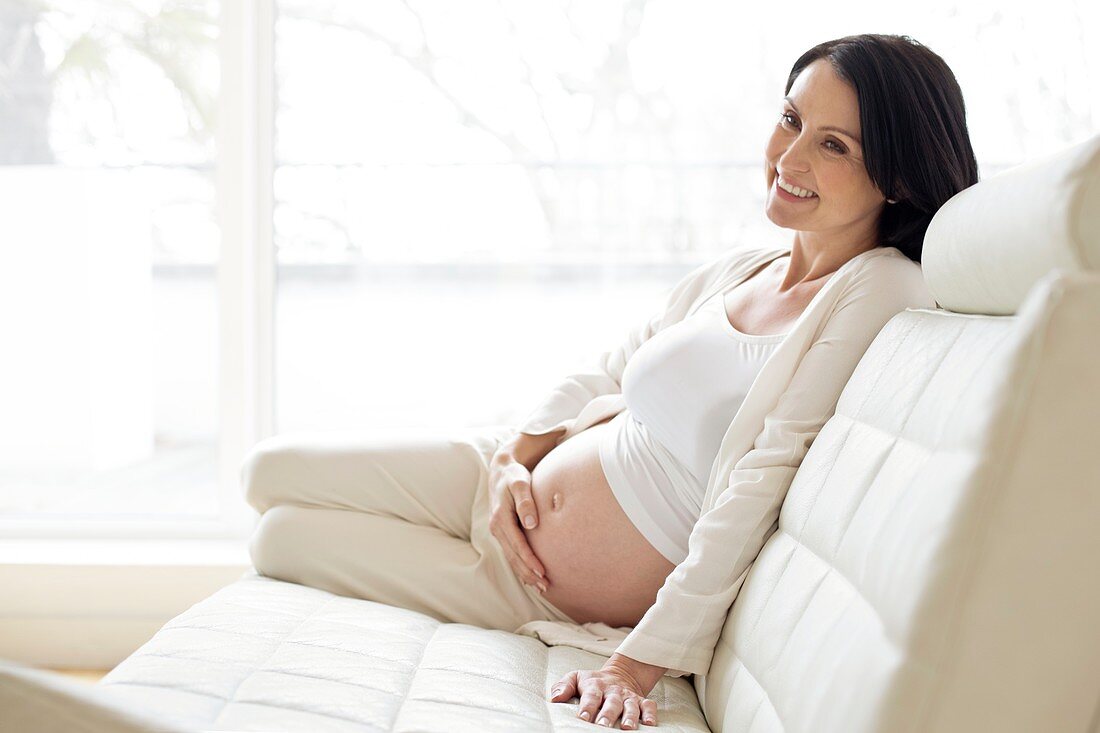 Pregnant woman on sofa touching tummy