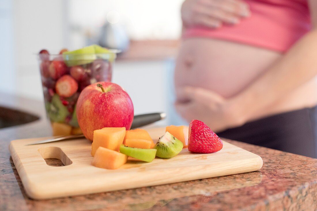 Freshly cut fruit on board with pregnant woman