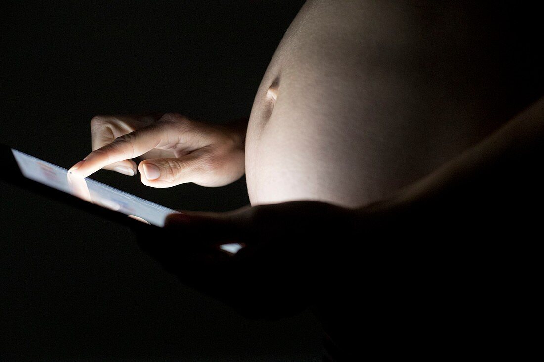 Pregnant woman using digital tablet in dark