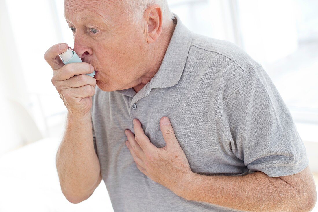 Senior man using inhaler, holding chest