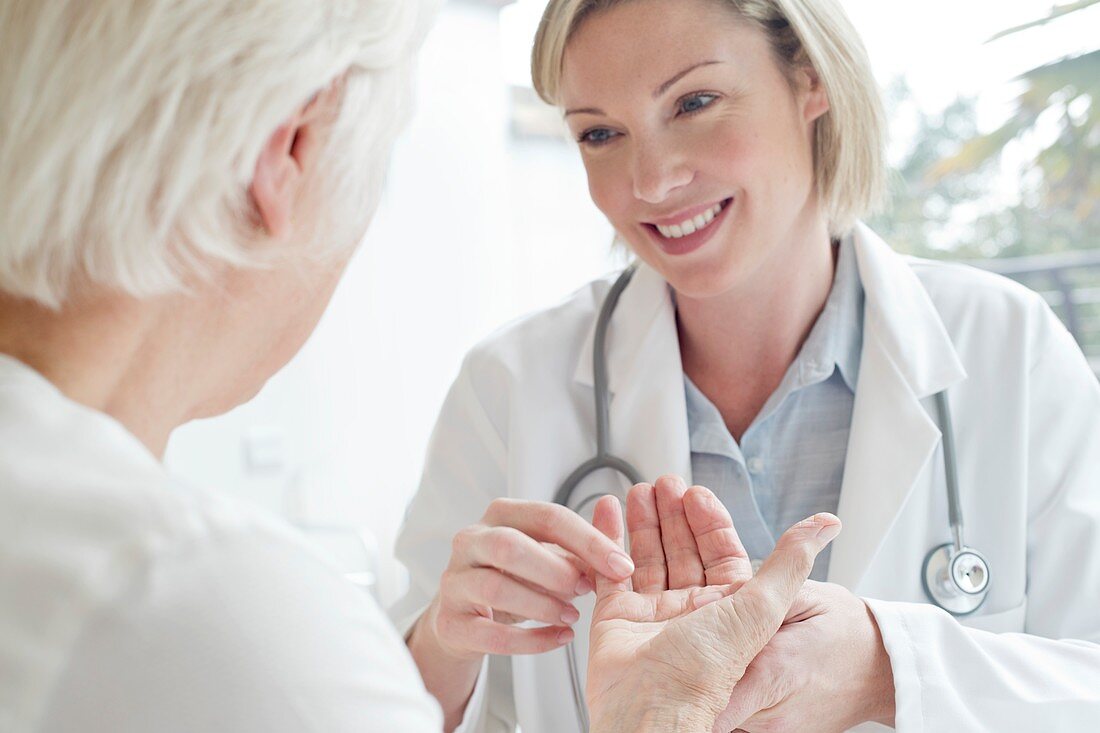 Female doctor examining senior patient's hand