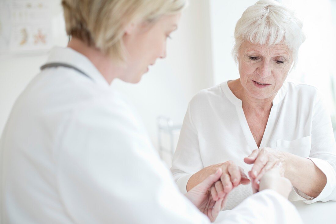 Female doctor examining senior patient's hand
