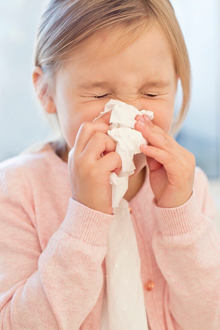 Young girl sneezing into tissue