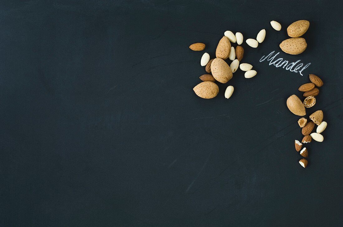 Almonds, whole and hulled, arranged around the German word for almond written in chalk on a blackboard