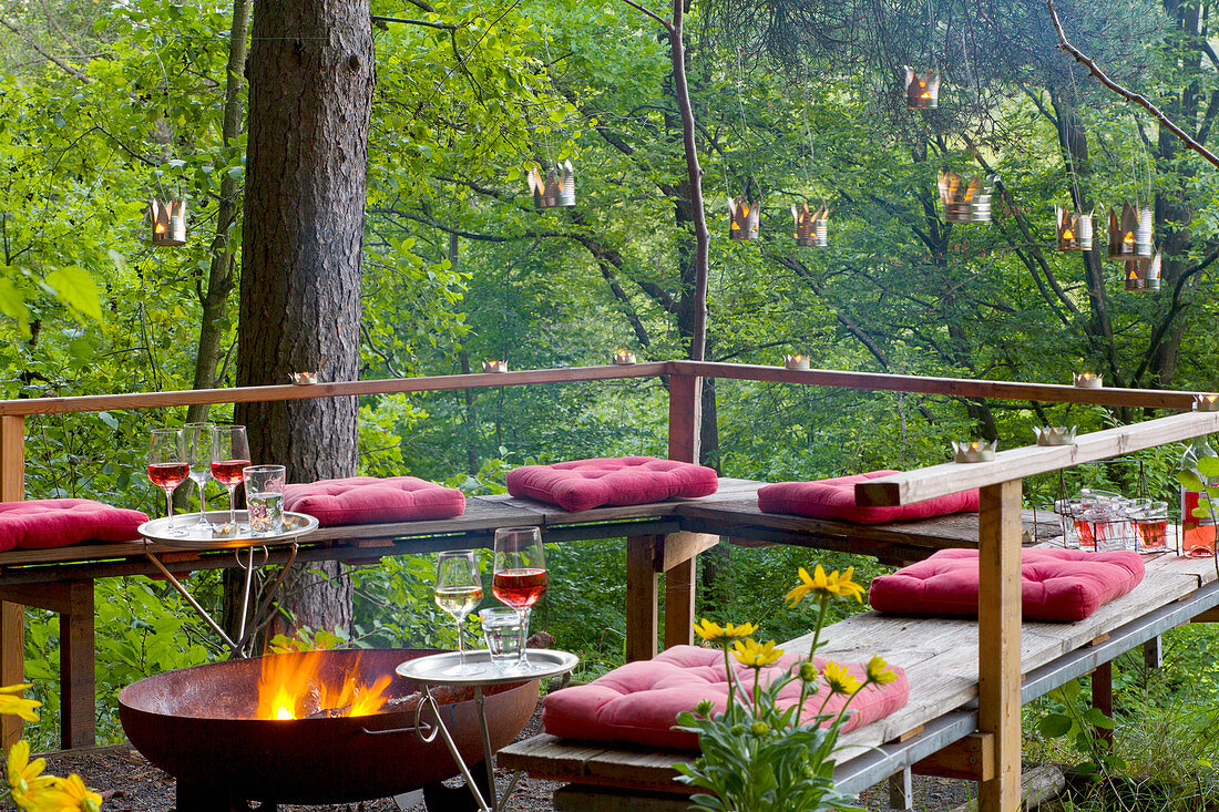 Bank und Feuerschale auf einer Naturterrasse mit aufgehängten, DIY-Sommerlichtern aus Metalldosen