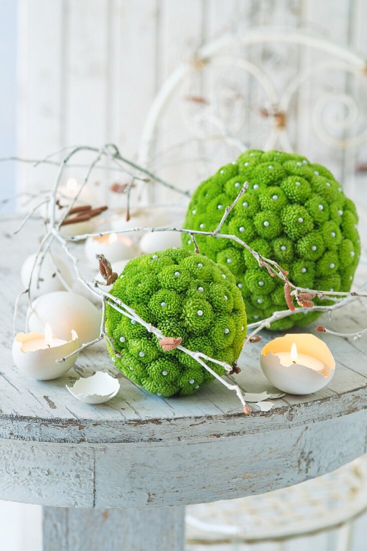 Balls of green flowers, white branches and candles in egg shells