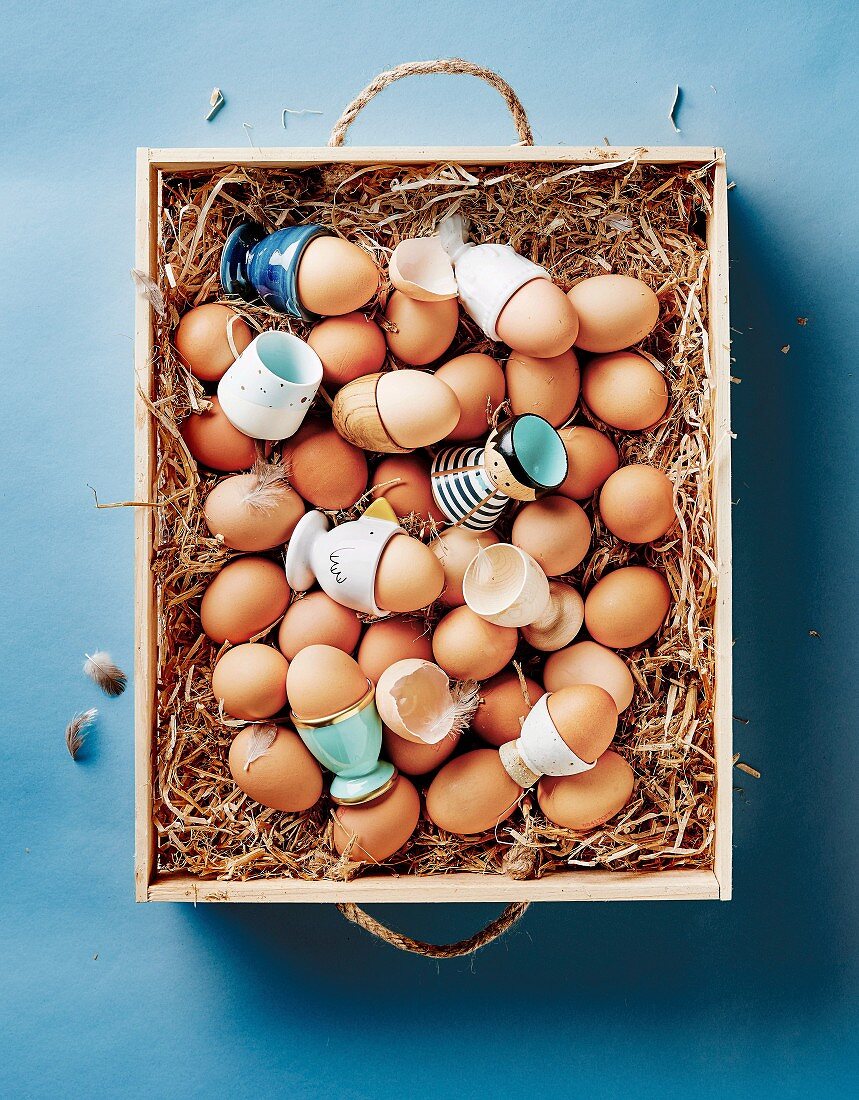 Braune Eier und Eierbecher in einer Holzkiste mit Stroh