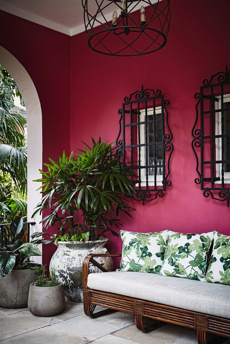 Sofa and plants on a veranda with a pink wall and window grilles