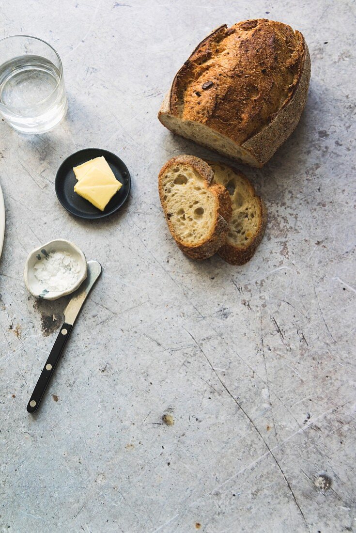 A sliced loaf of sourdough bread with butter, salt and a glass of water