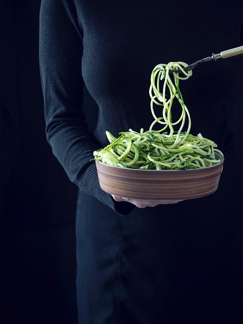 Frau hält Schüssel mit rohen Zucchinispaghetti