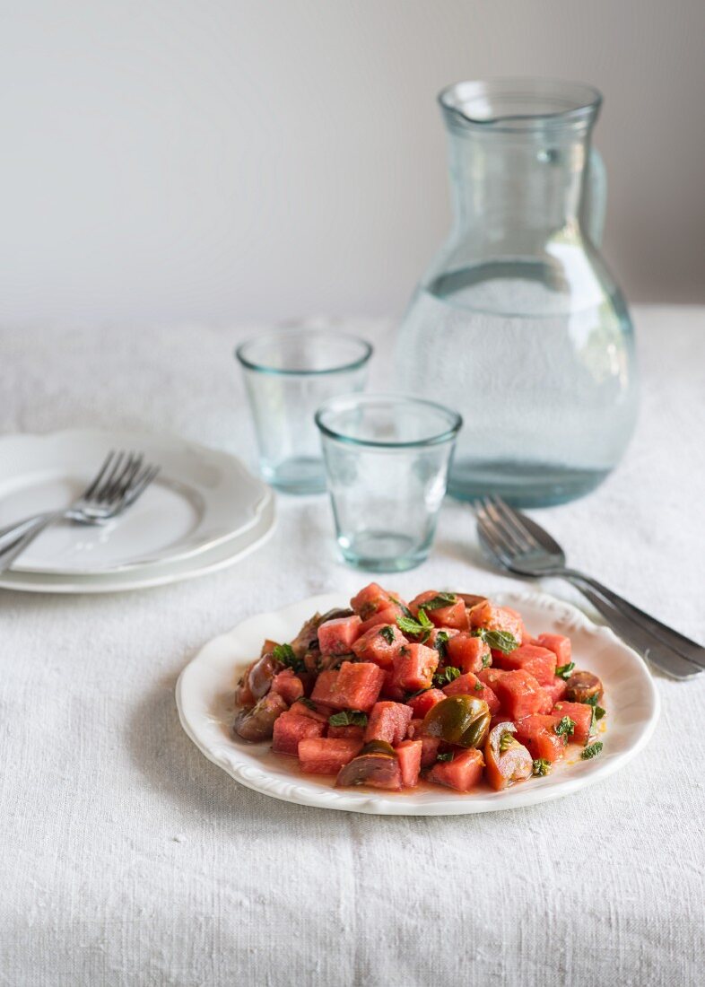 Tomato and watermelon salad on a white tablecloth with a jug and glasses