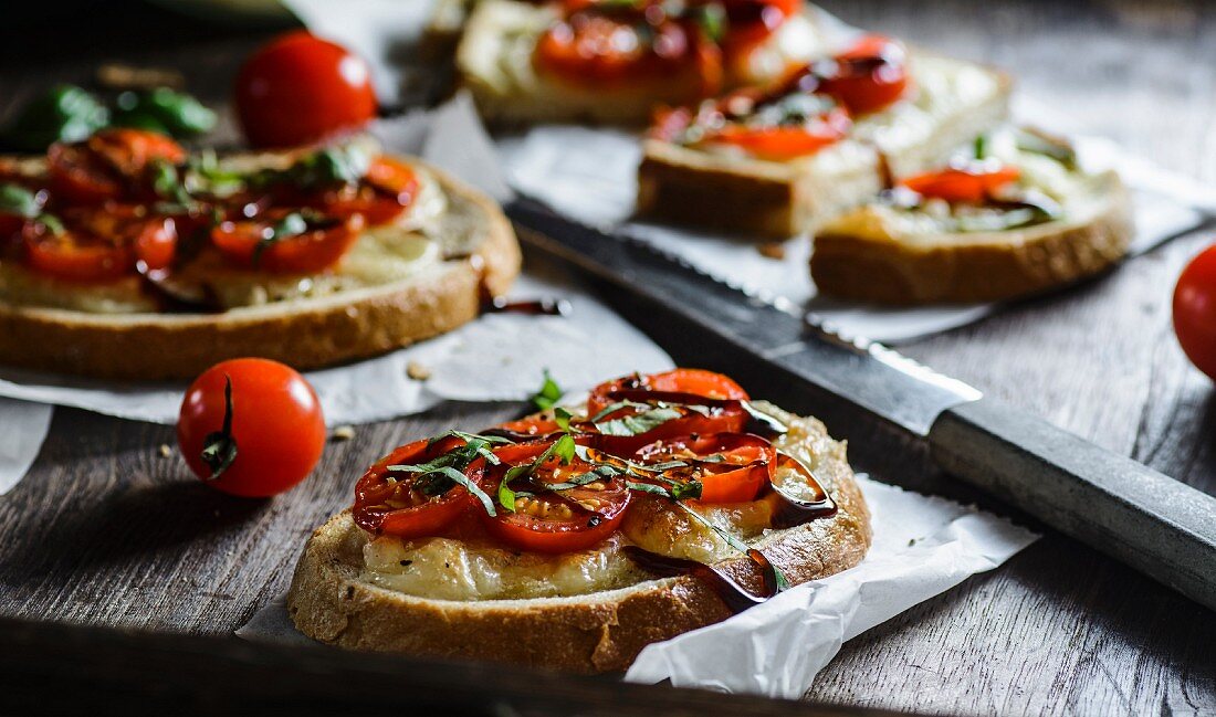 Slices of bread topped with cherry tomatoes, mozzarella and balsamic vinegar