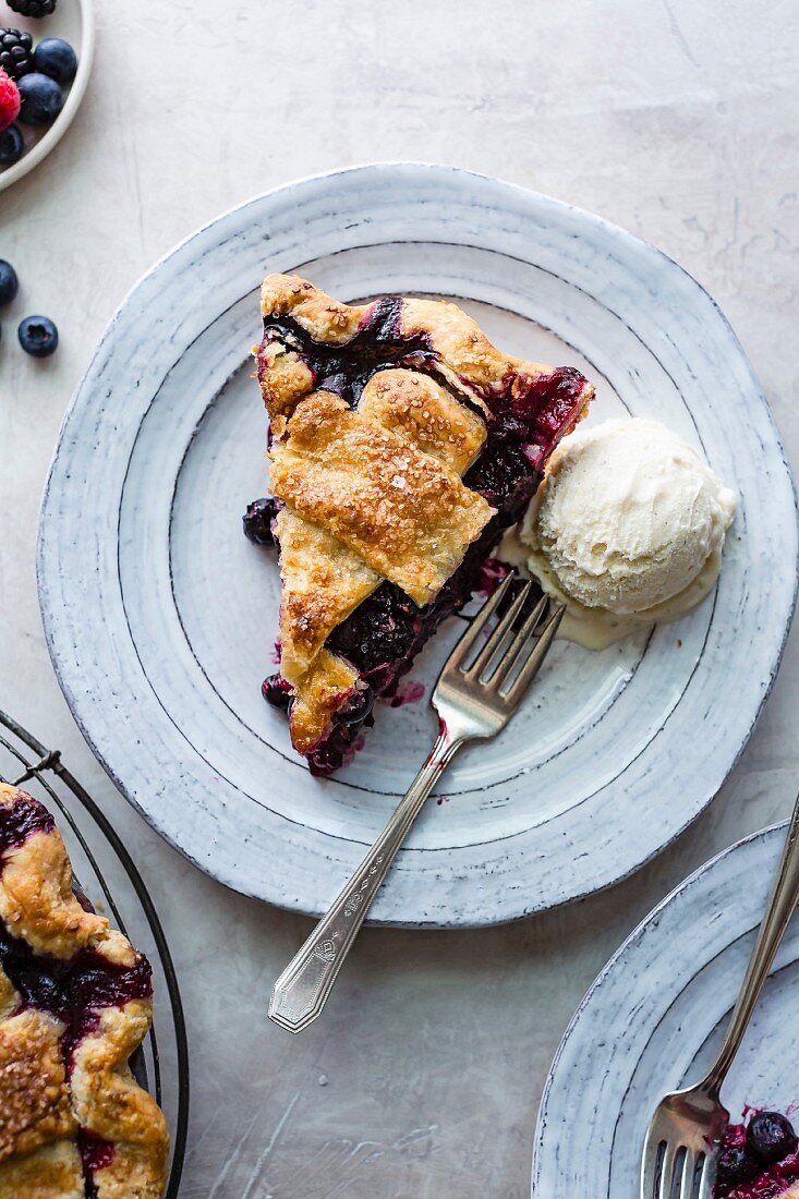 A slice of berry pie with vanilla ice cream on a plate