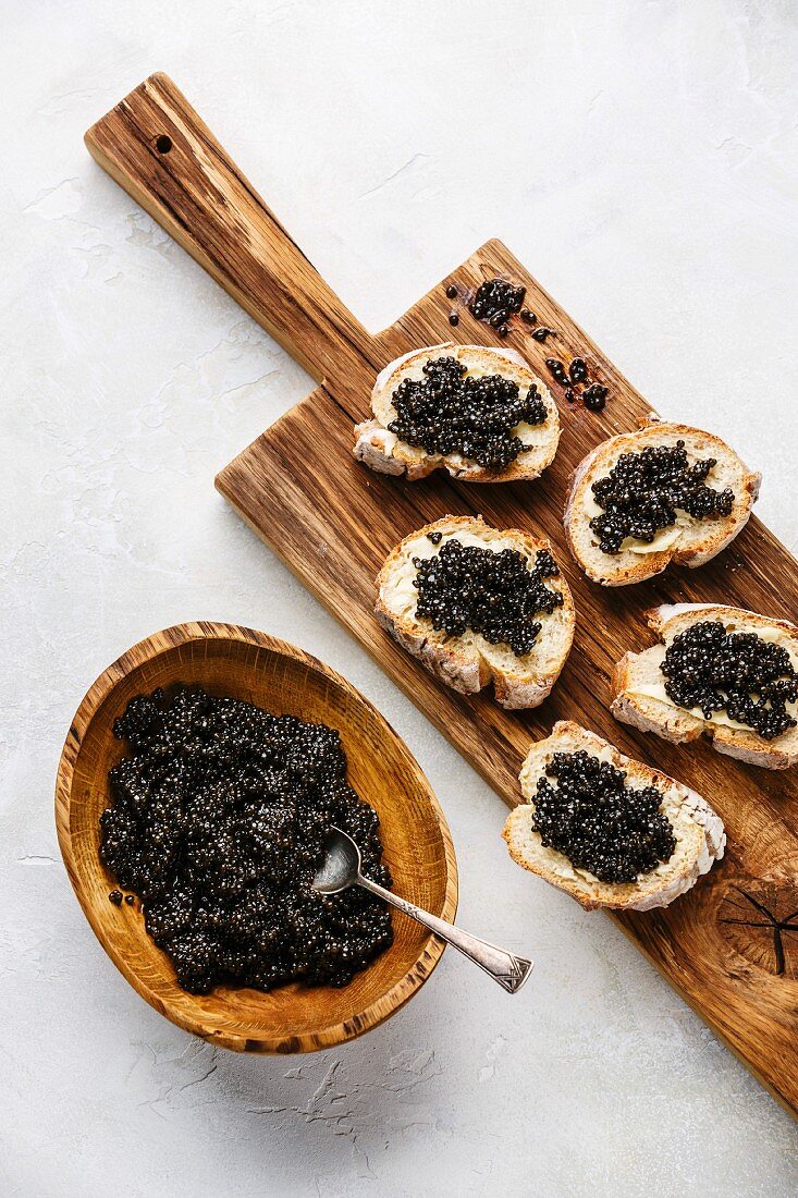 Schwarzer Kaviar in Holzschale und auf Weissbrotscheiben