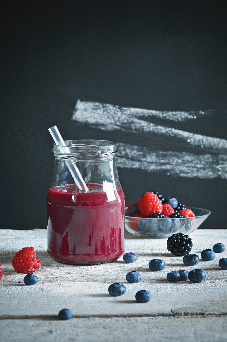 Smoothie mit Heidelbeeren, Himbeeren, Brombeeren auf rustikalem Holztisch