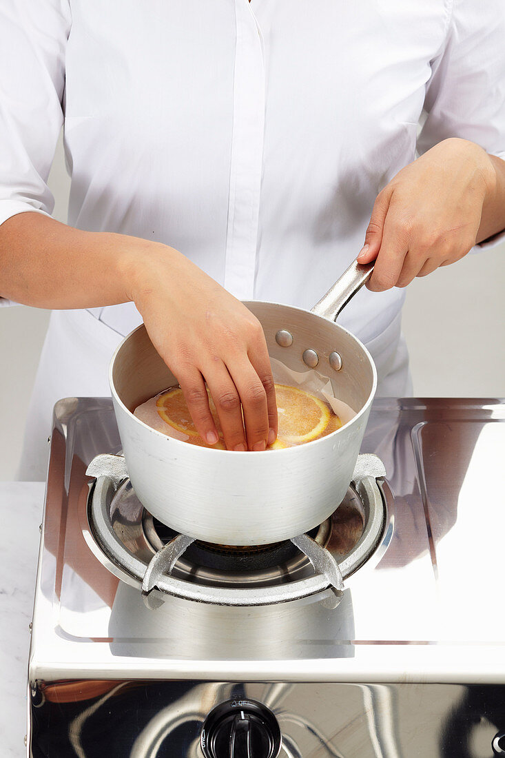 Chef adds orange slices to a sauce pan and covers them with baking paper