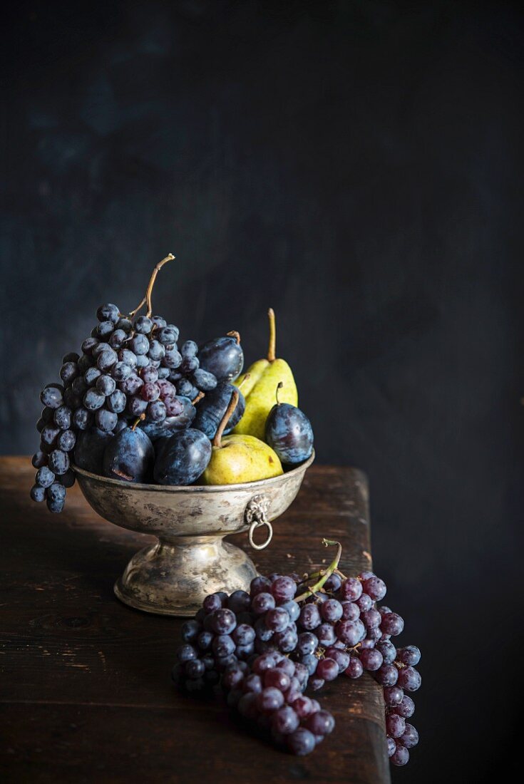 Grapes, plums and pears in a metal bowl on a wooden table