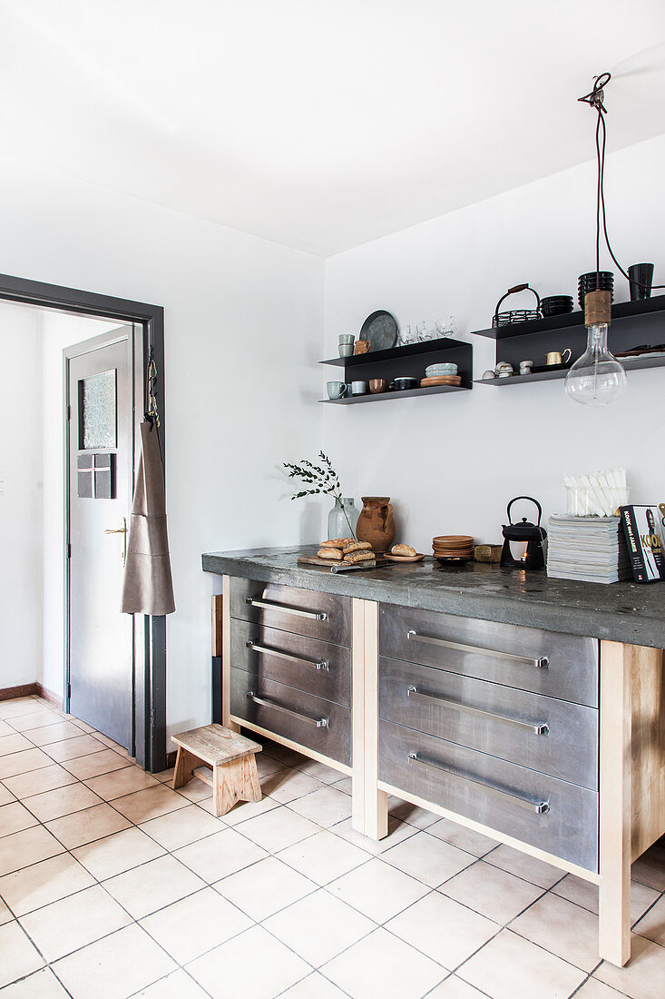 Base units with drawers and concrete worksurface below black wall-mounted shelves in kitchen