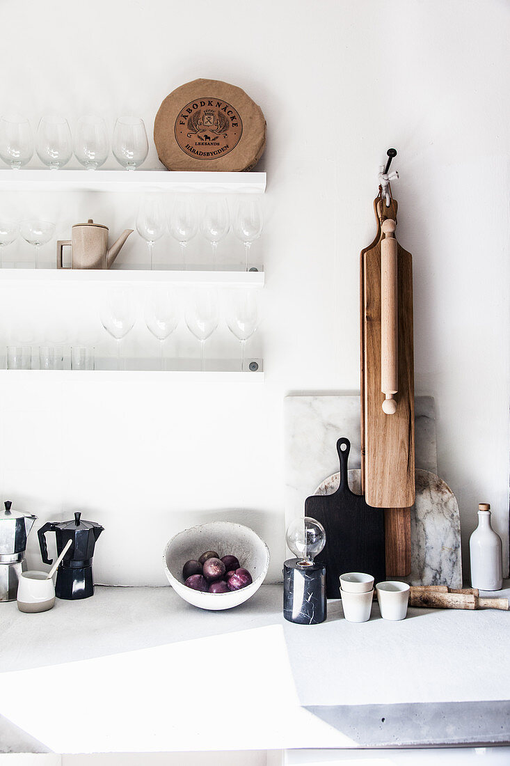 Kitchen utensils on worksurface below shelves of glasses