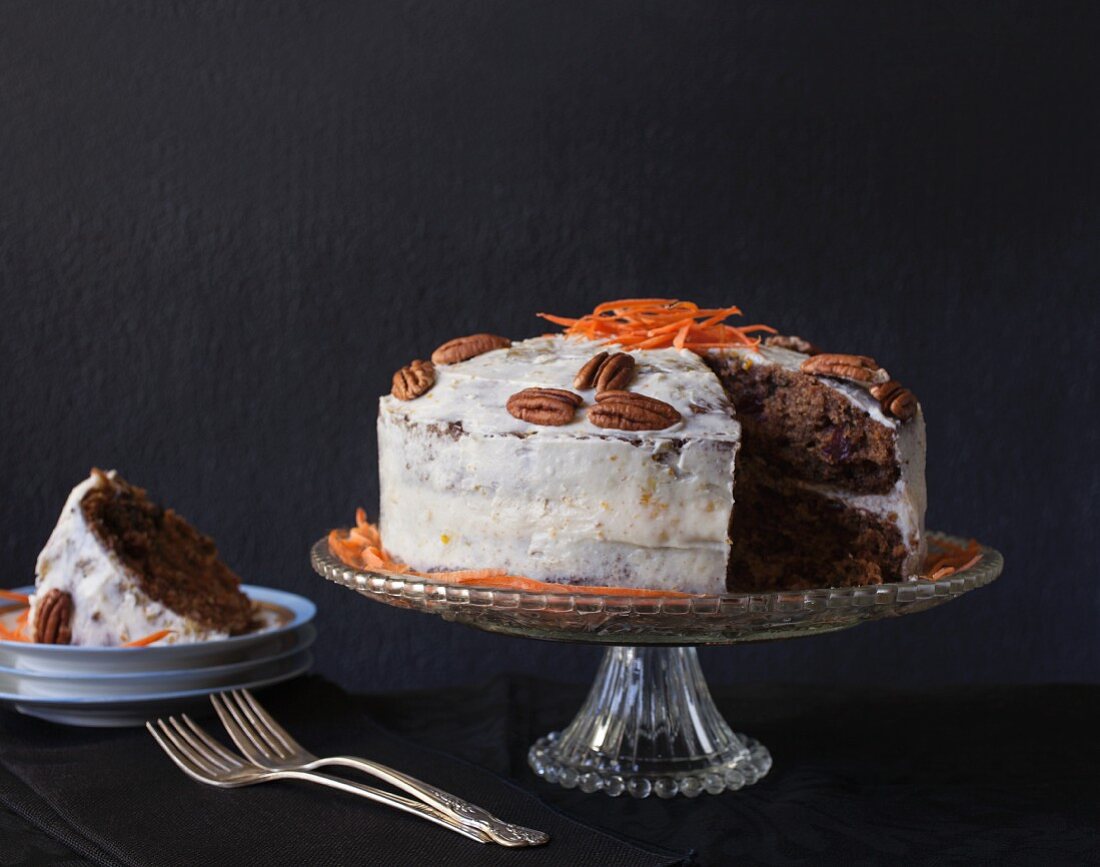 Carrot cake with pecan nuts and a piece missing on a cake stand