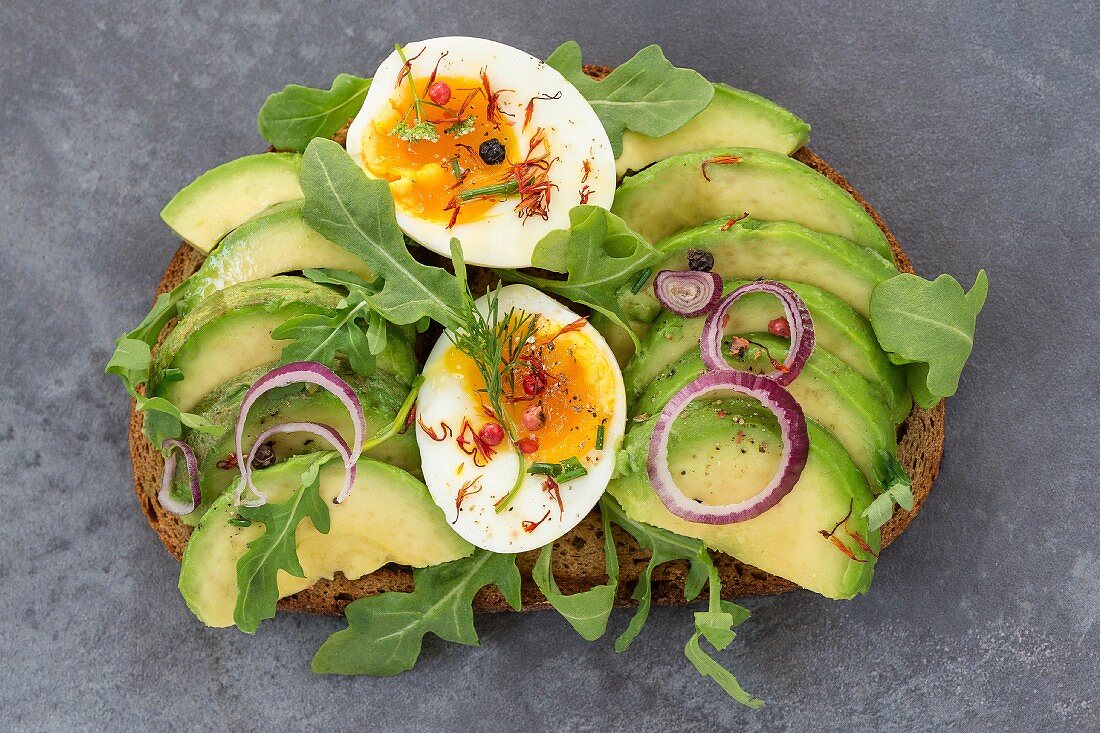 Bread topped with avocado, egg, rocket and red onion
