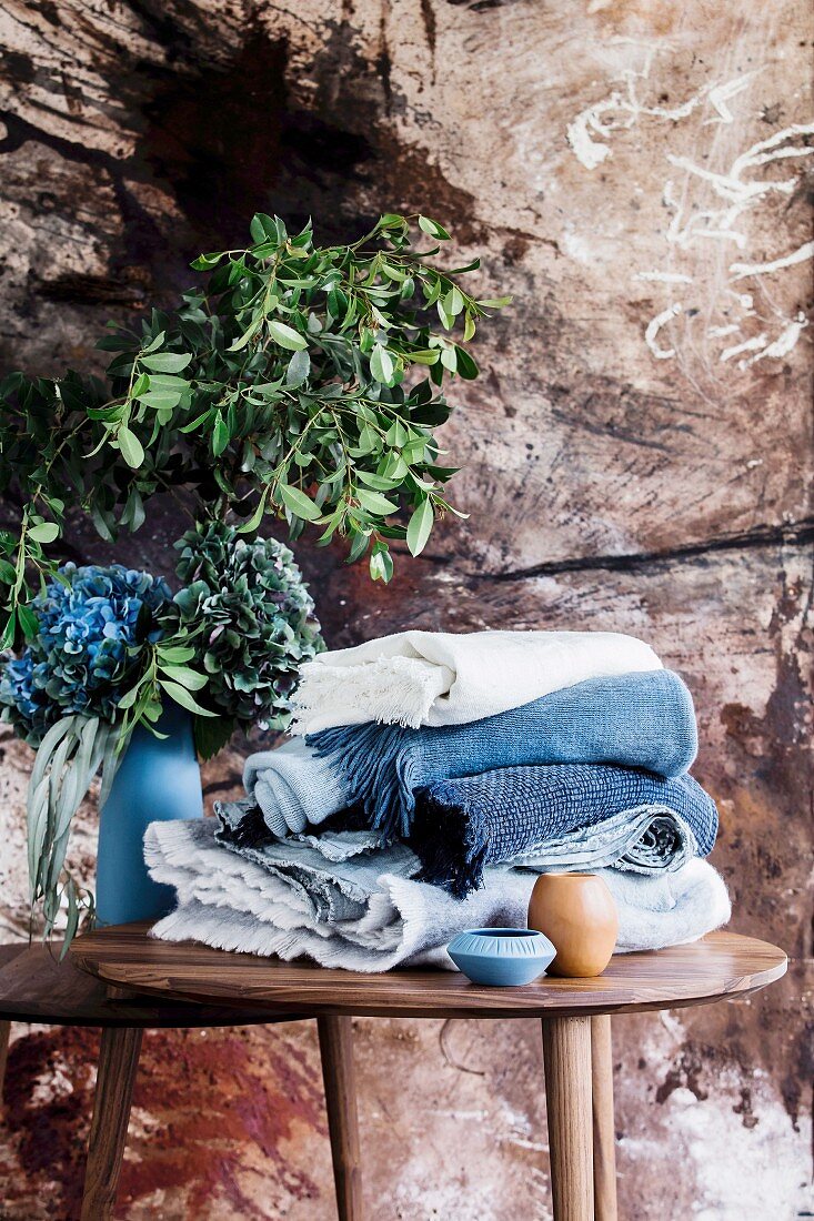 Folded blankets in shades of blue on a wooden table with flowers