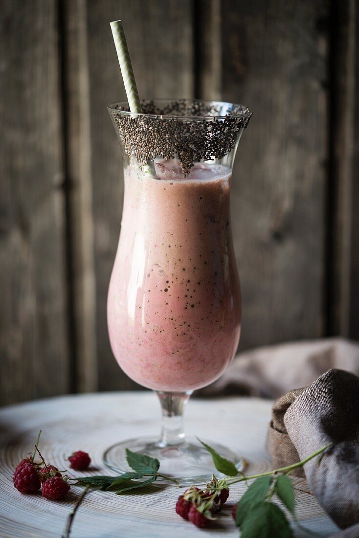 A vegan raspberry smoothie in a glass with chia seeds around the rim