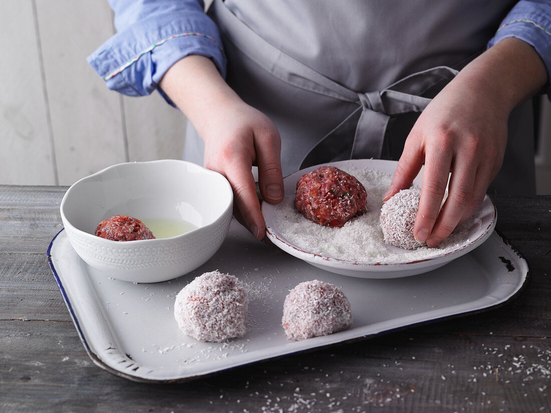 Meatballs being rolled in coconut flakes