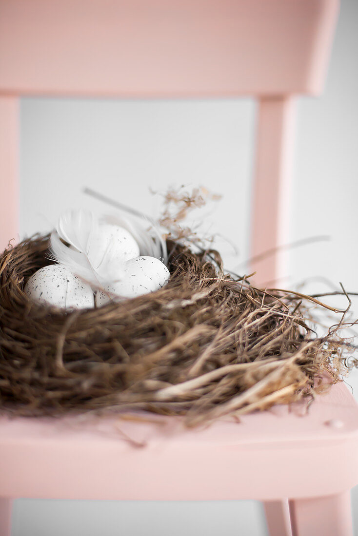 Osternest mit gesprenkelten Eiern auf rosa Stuhl